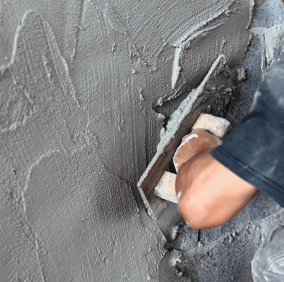 Main d'ouvrier appliquant du ciment gris texturé sur un mur avec une truelle. Surface d'enduit frais et rugueux en gros plan.
